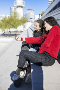 Female friends sitting with skateboards on staircase in city