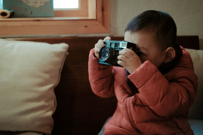 Close-up of boy photographing with camera while sitting on sofa at home