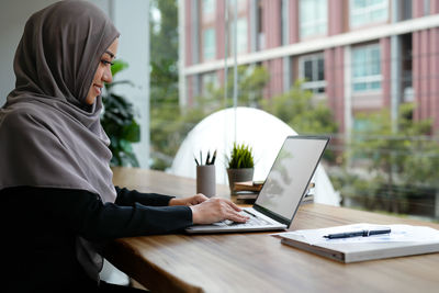 Rear view of woman using laptop at office