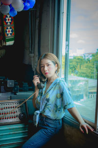 Young woman looking away while sitting on window