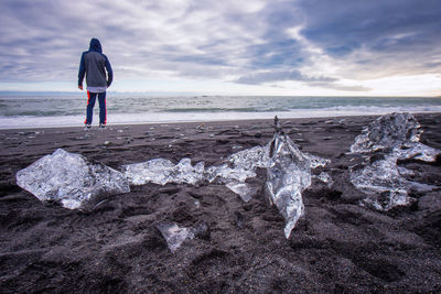 Rear view of man standing against icebergs at beach