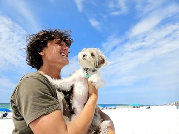 Happy millennial guy on beach hugging cute puppy.
