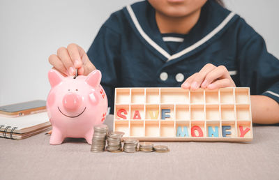 Little girl putting coin into piggy bank for saving with pile of coins on table and show save money 