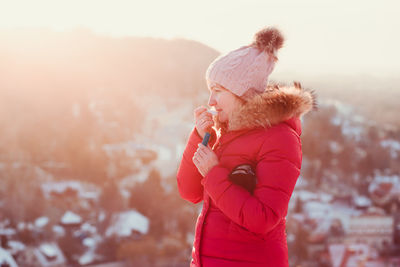 Woman applying lipstick while standing against mountain during winter