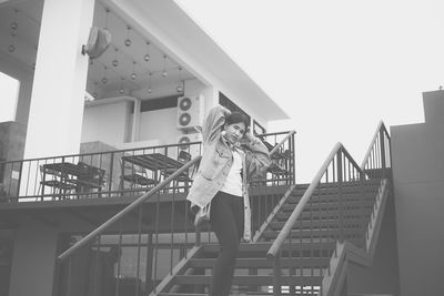 Portrait of young woman standing on steps against clear sky