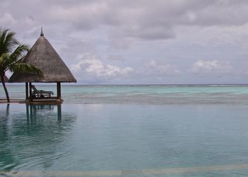 Gazebo at sea against cloudy sky