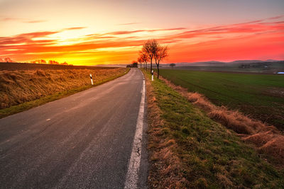 Road amidst agricultural field against sky during sunset