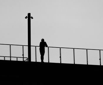 Silhouette of person standing by railing against clear sky