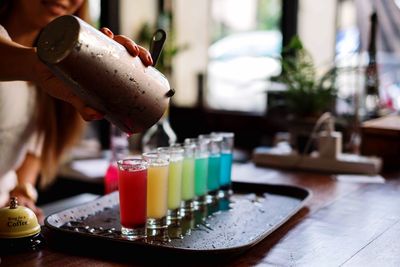 Midsection of female bartender pouring colorful cocktails at counter