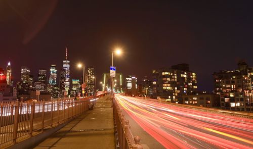 Light trails on road amidst buildings against sky at night