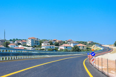 Road by buildings against clear blue sky