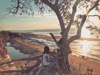 Woman sitting on tree trunk by sea