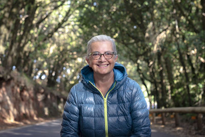 Portrait of smiling senior woman standing on road amidst forest
