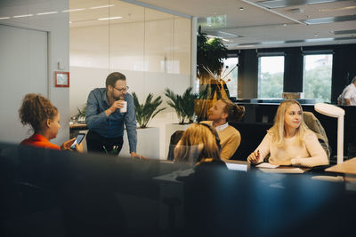 Multi-ethnic colleagues discussing at office seen from glass