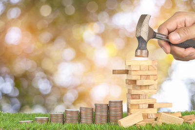 Cropped hand holding hammer over coins and dominos against lens flare