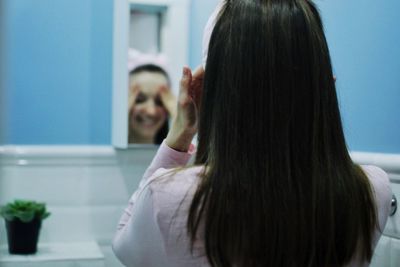 Rear view of woman standing in front of mirror at home