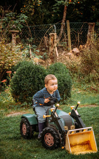Portrait of boy sitting on toy tractor by plants