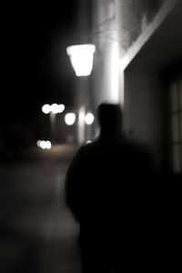 Rear view of silhouette man standing on illuminated street at night