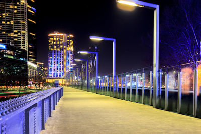 Illuminated street amidst buildings against sky at night