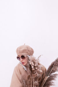 Woman wearing hat holding plant against white background