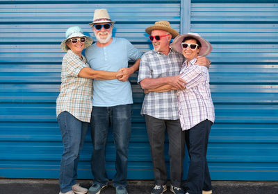 Portrait of smiling friends wearing sunglasses and hats against wall