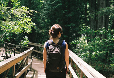 Rear view of woman standing on footbridge in forest