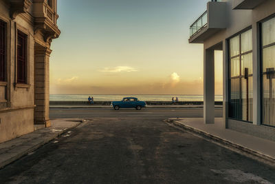 Vintage car on road by sea against sky during sunset
