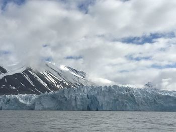 Scenic view of sea by snowcapped mountains against sky