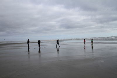 People on shore at beach against cloudy sky