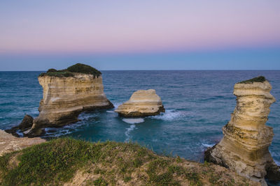 Rock formations at sea against sky during sunset 