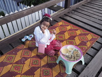 High angle portrait of cute girl sitting at wooden pier with food outdoors