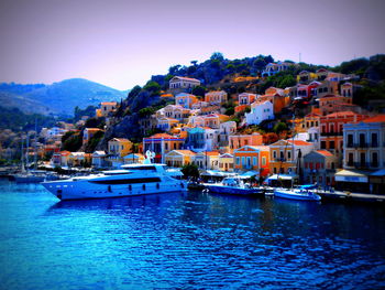 Boats moored in sea by townscape against sky