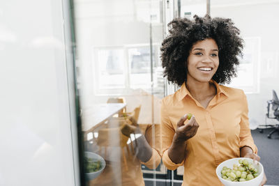 Smiling young woman holding bowl with grapes in office