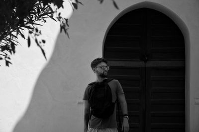 Young man looking away while standing against wall