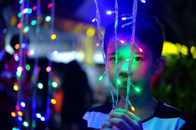 Portrait of boy holding illuminated string lights at night