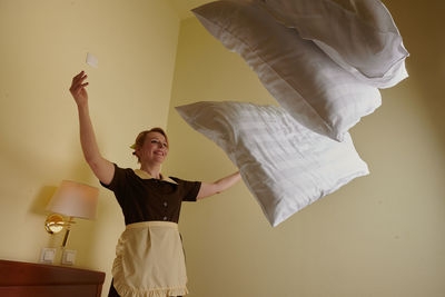 Portrait of young woman with arms raised standing against wall