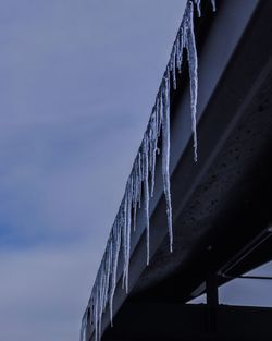 Low angle view of icicles on roof against cloudy sky