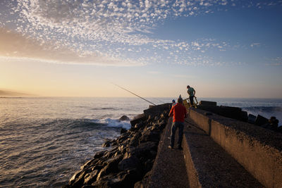 Rear view of men on wall fishing in sea