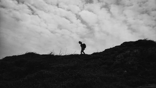 Low angle view of silhouette young woman walking on hill against cloudy sky