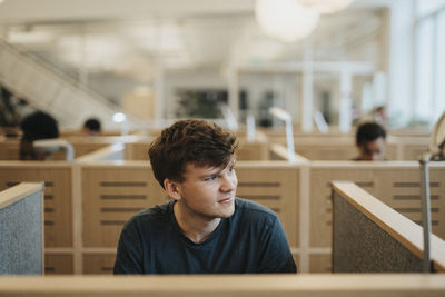 Smiling young man looking away while sitting in library at university