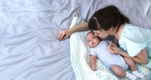 Young mom with her 2 month old newborn baby lying in bed at home. happy moments. copy space.