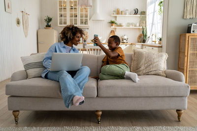 Happy african american family mother and son enjoy weekend at home rest on sofa with gadgets