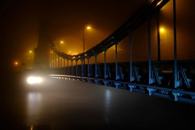 Illuminated bridge over river against sky at night