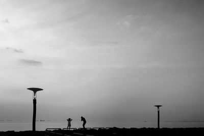 Silhouette people on street by sea against sky