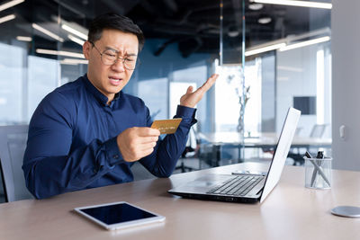 Portrait of young man using laptop at office