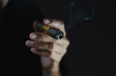 Midsection of man holding cigarette against black background