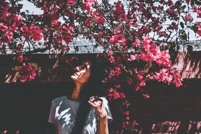 Woman standing by pink cherry blossom against trees