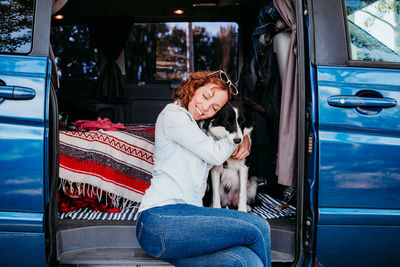 Woman embracing dog while sitting at entrance of camper trailer