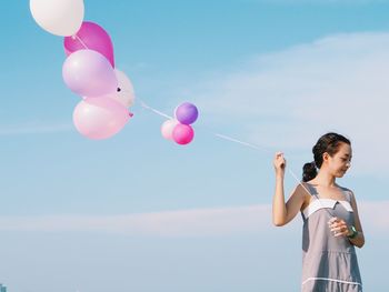 Low angle view of girl holding balloons against blue sky