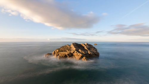 Rocks in sea against sky during sunset